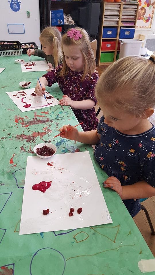 Three children painting at a table in a classroom