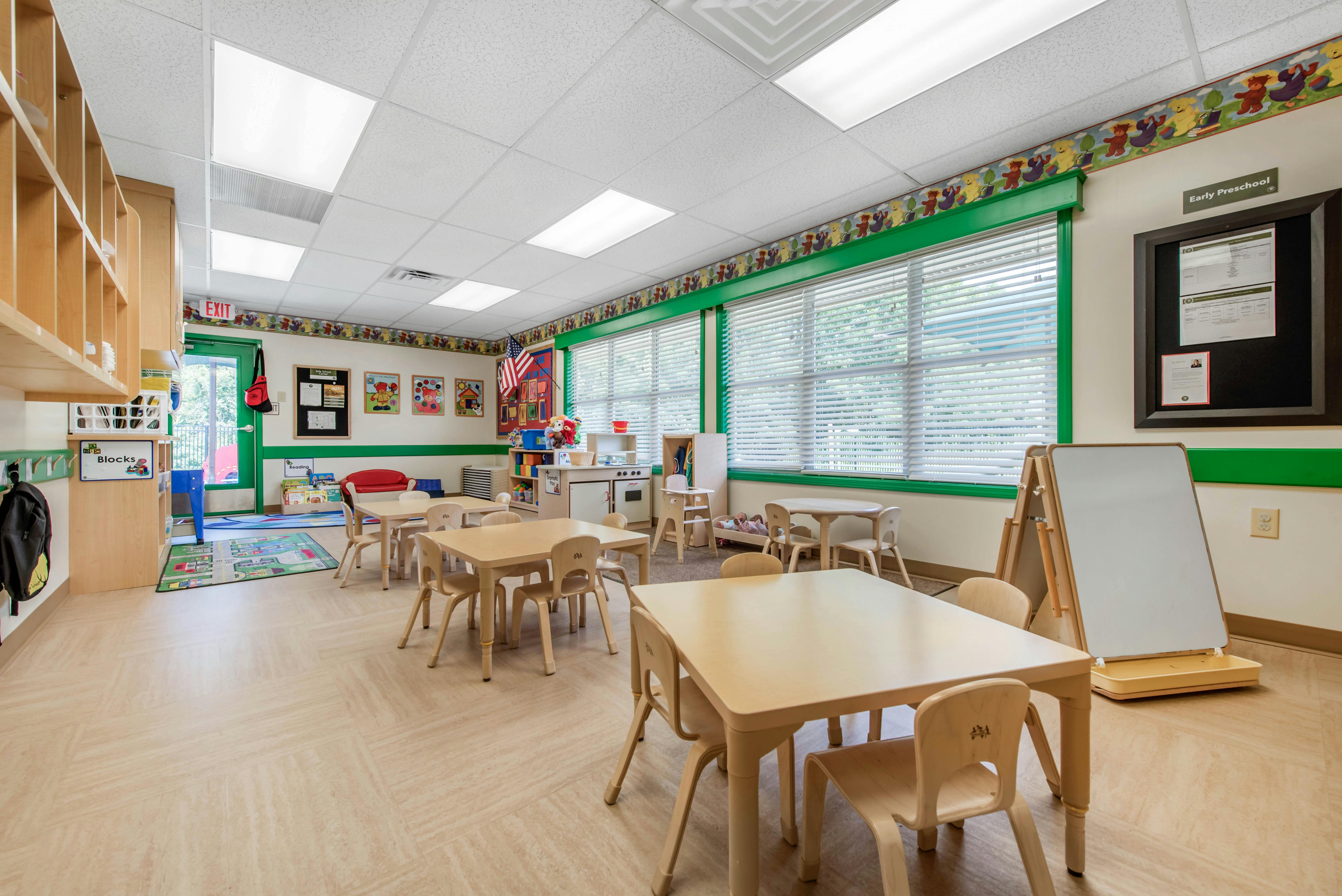 Classroom with small tables and chairs, play kitchen, and window blinds