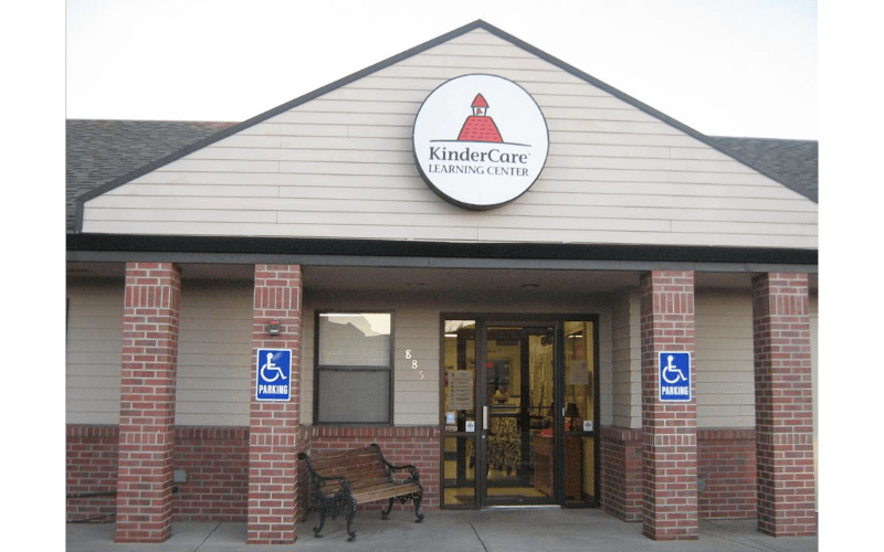 KinderCare Learning Center sign on a building with brick pillars and a bench