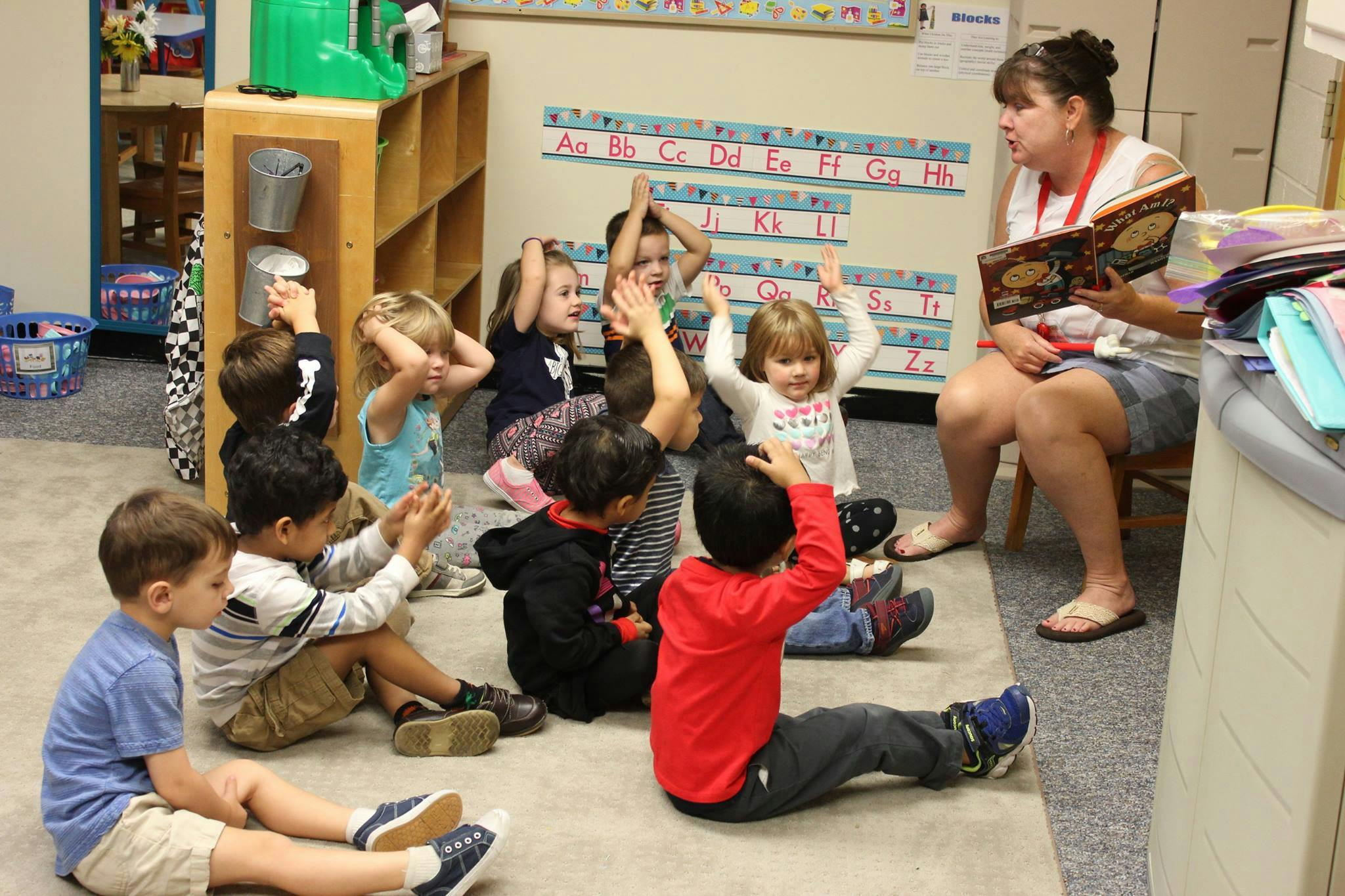 Adult reading to children in a classroom, children raising hands