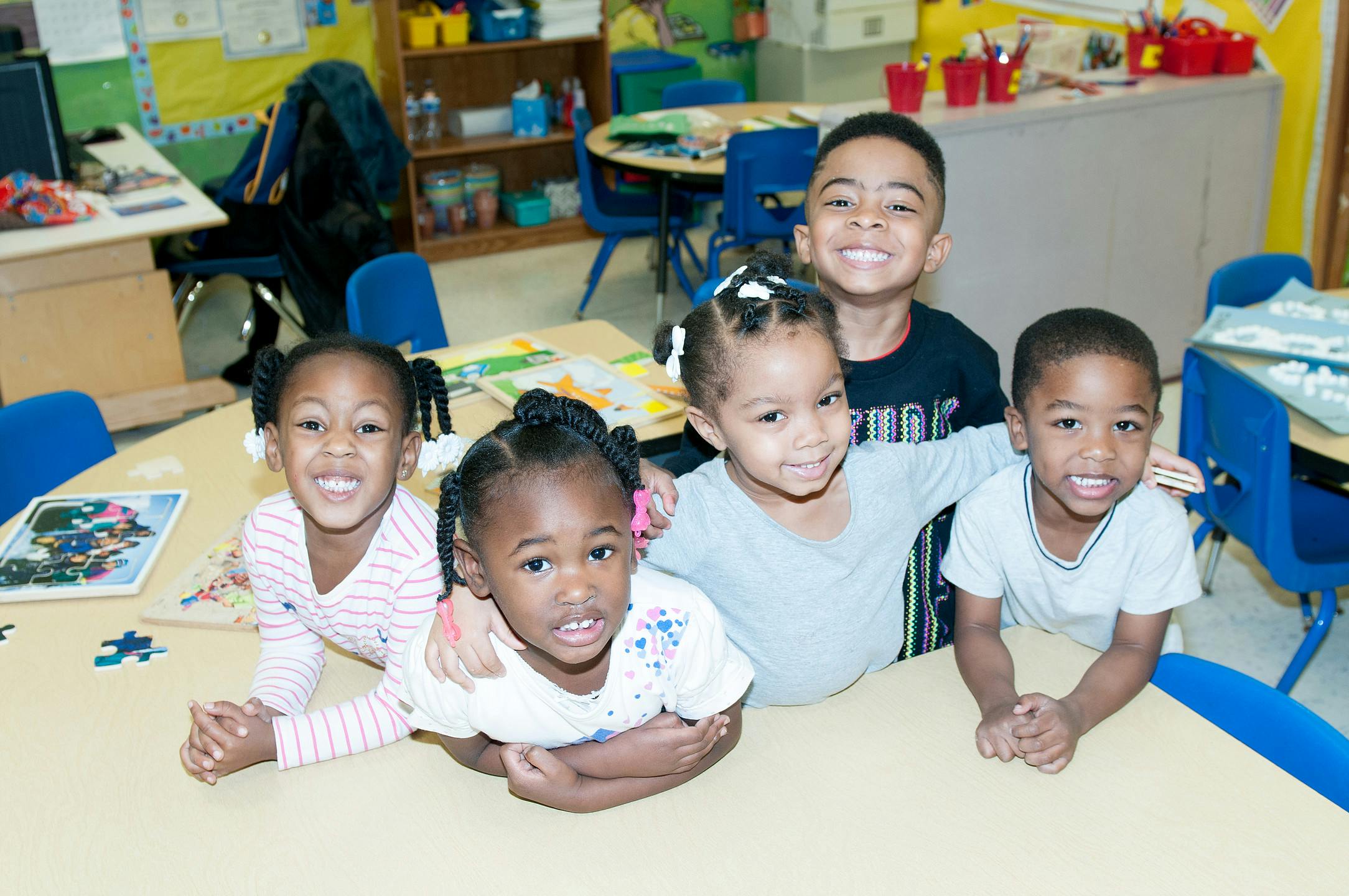 Five children smiling at a table in a classroom