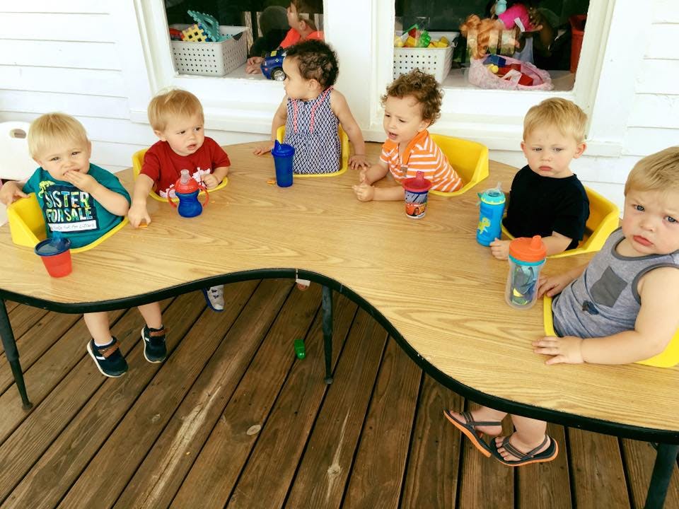 Multiple children sitting at a curved table with sippy cups