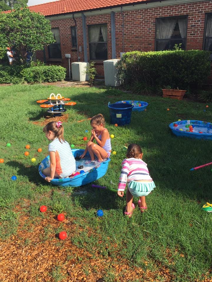 Children playing in a yard with small pools and colorful balls