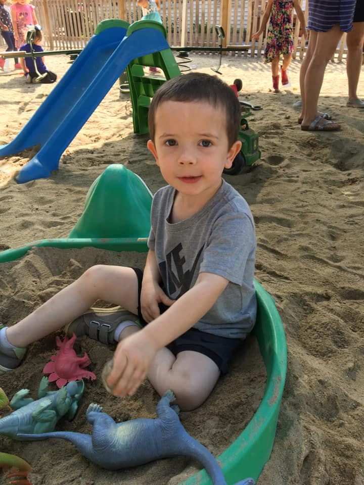 Child sitting in a sandbox with toys