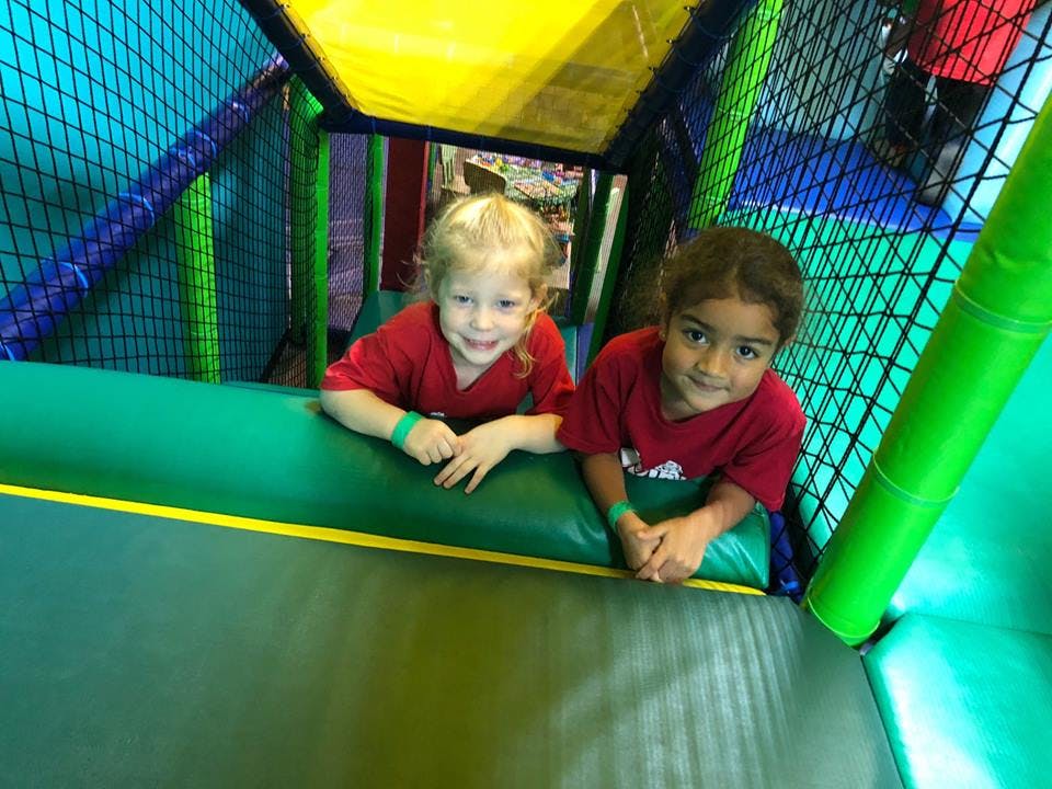 Two children in red shirts looking up from inside a play structure