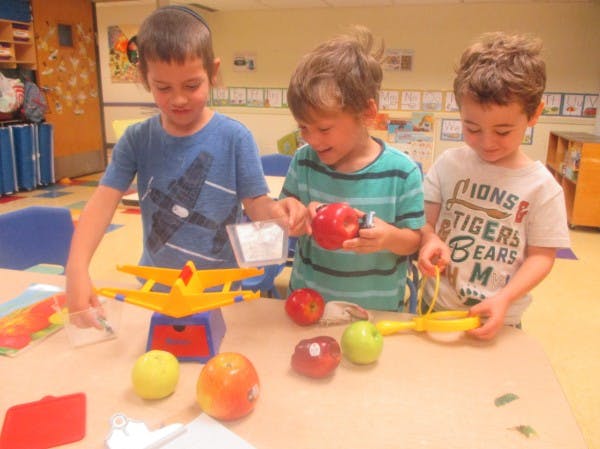 Three children playing with apples and a toy scale