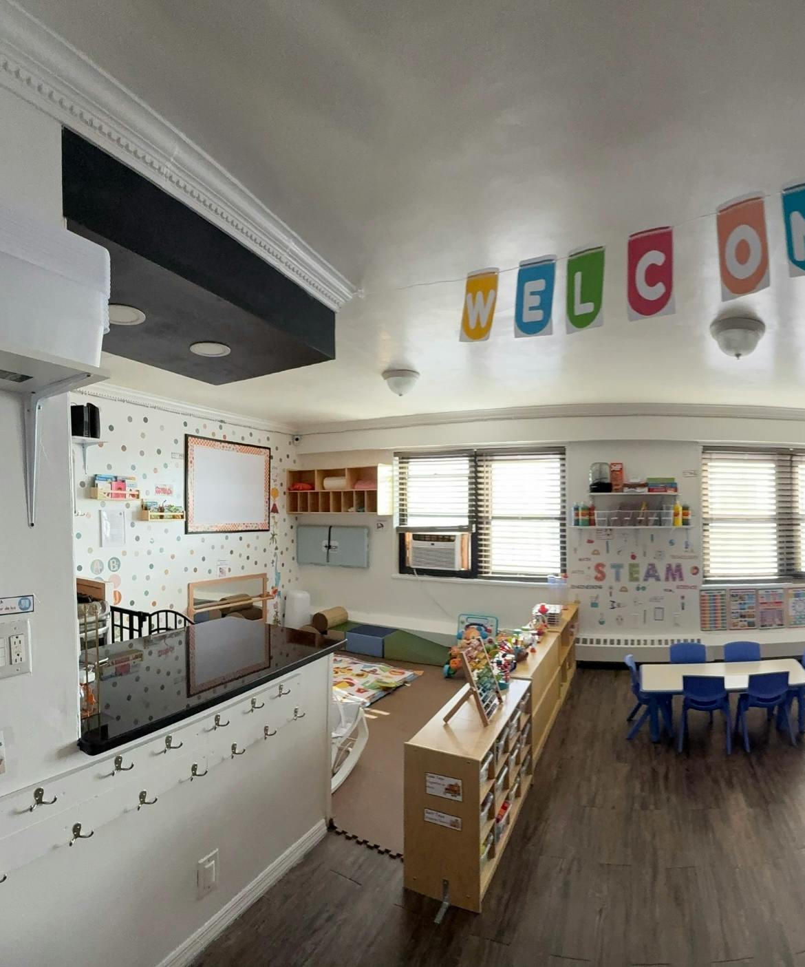 A colorful classroom with tables, chairs, toys, and a "WELCOME" banner