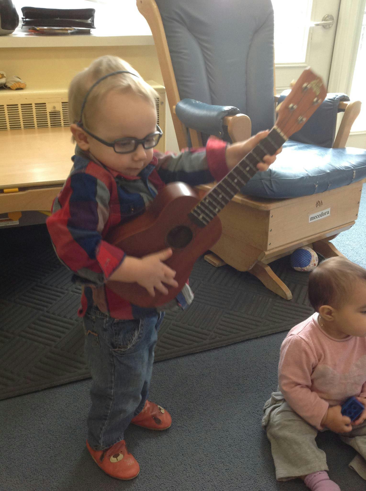 Child wearing glasses and playing a ukulele