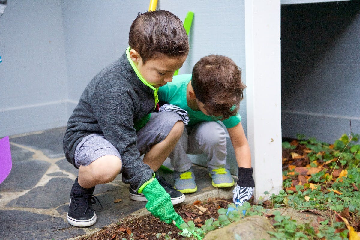 Two children wearing gloves, crouching and tending to plants