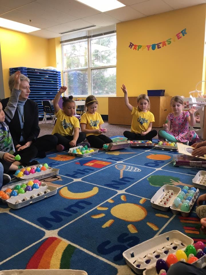 Adult and children sitting on a rug with colorful plastic eggs