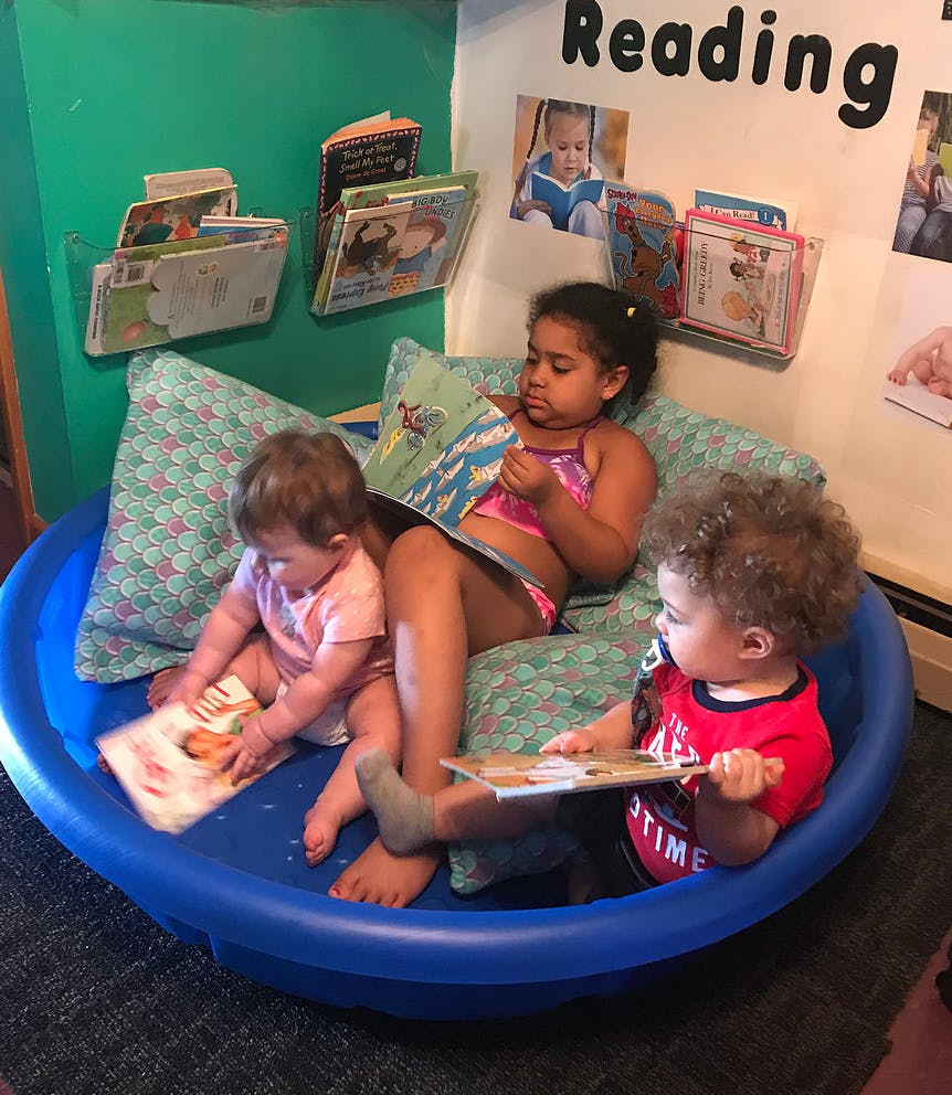 Three children sitting in a blue basin reading books