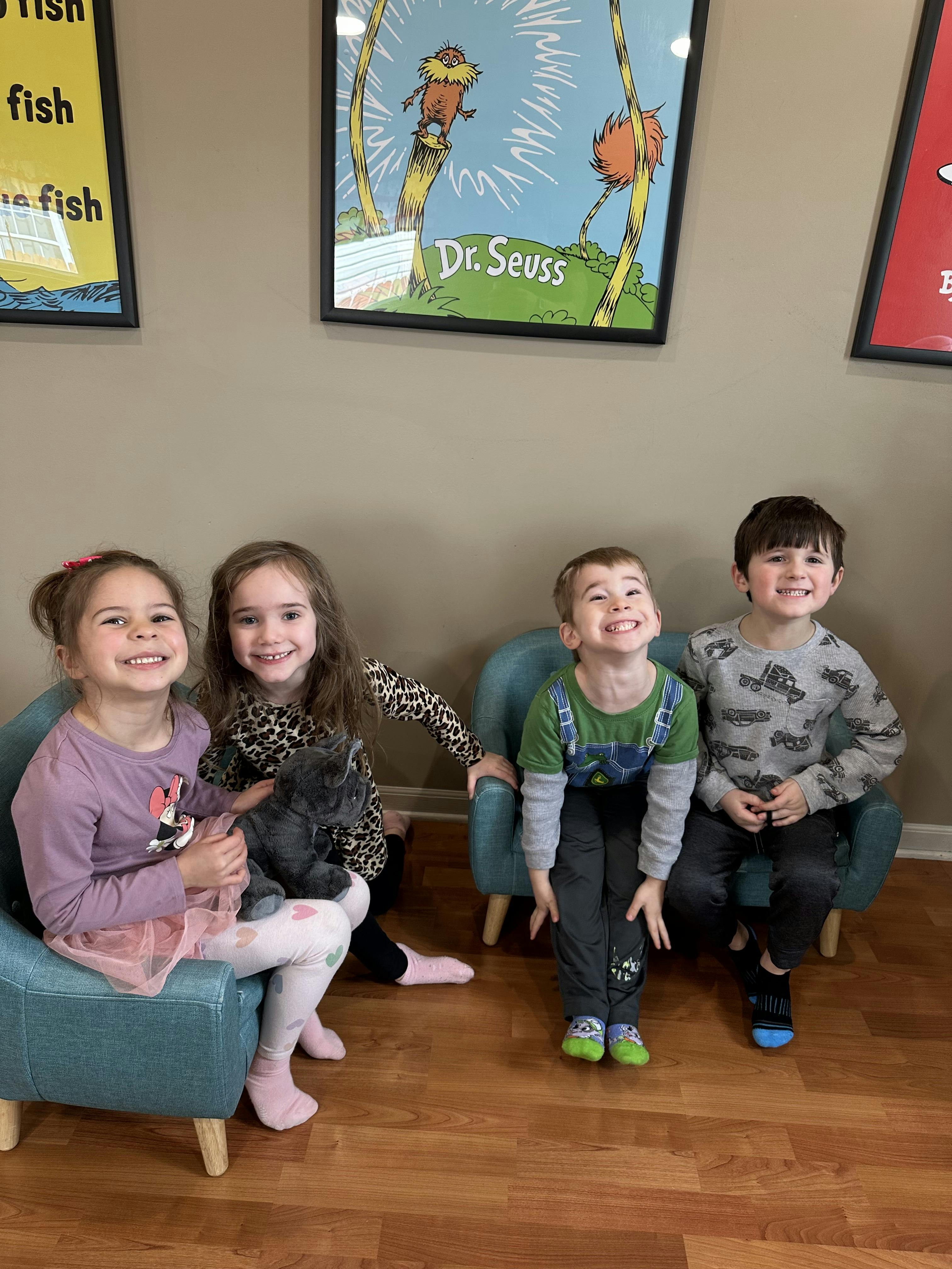 Four children sitting on small chairs with a cat