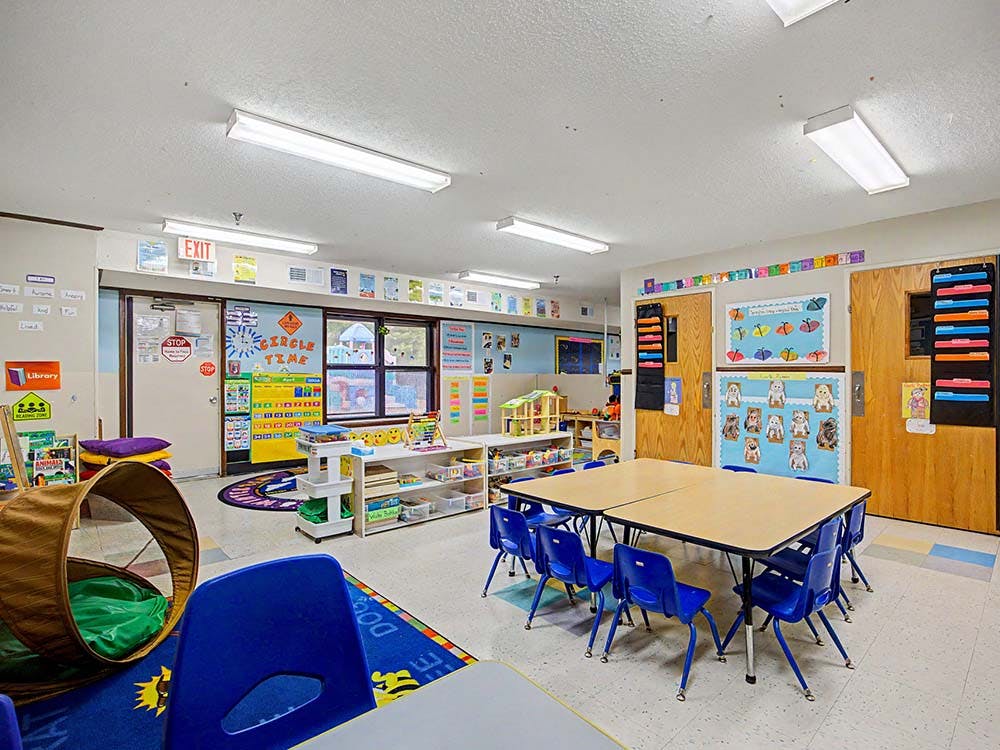 An empty classroom with small tables and blue chairs