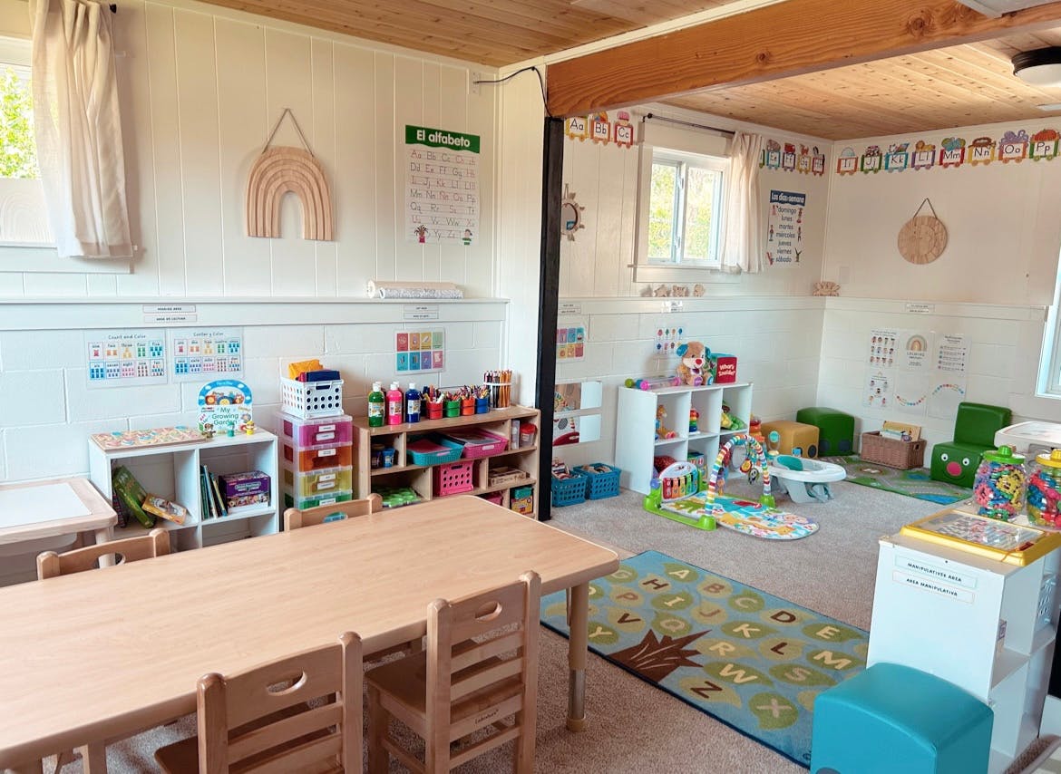 Classroom with small tables and chairs, shelves with toys and books