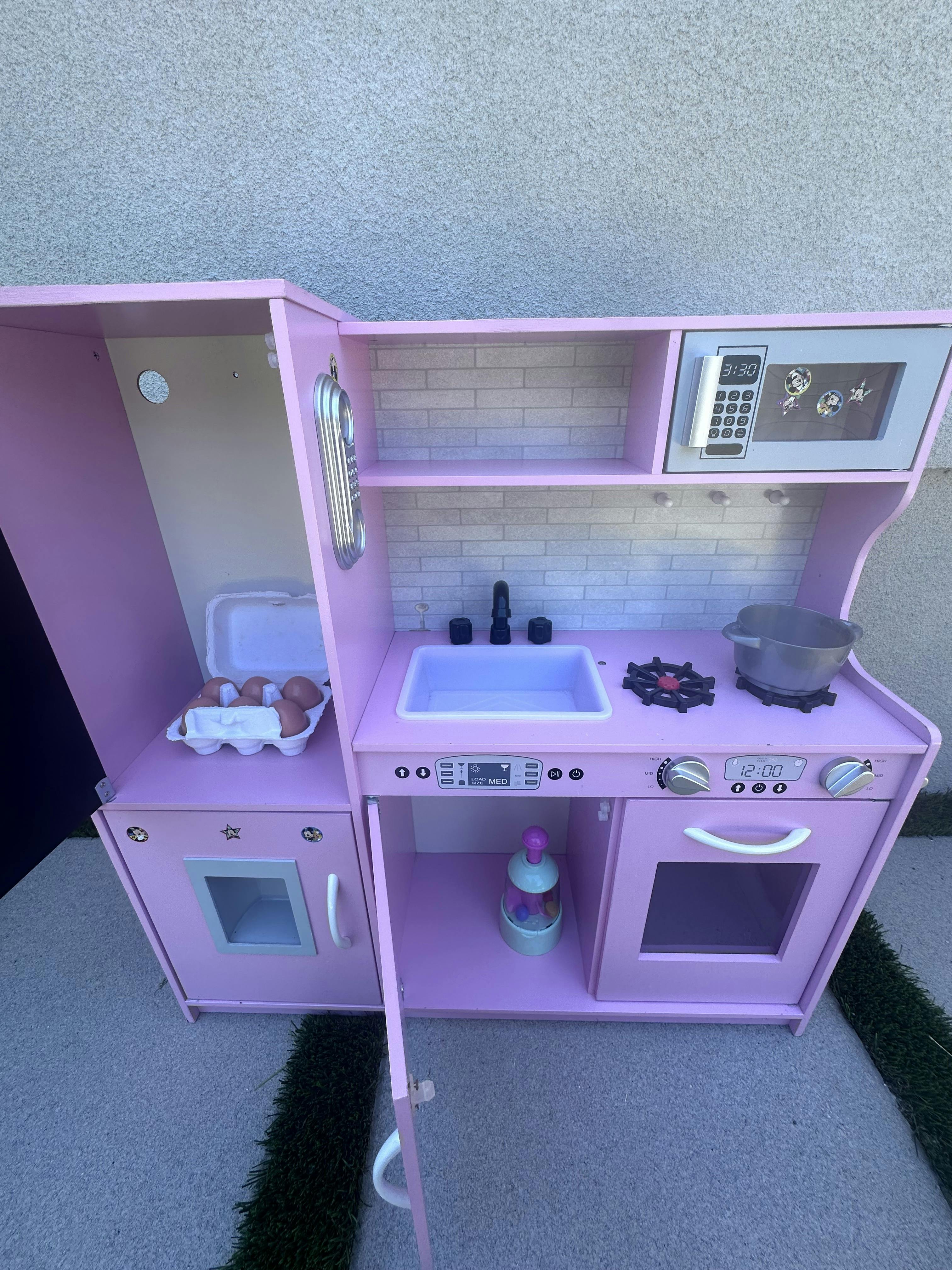 Pink toy play kitchen with a sink, stove, and microwave
