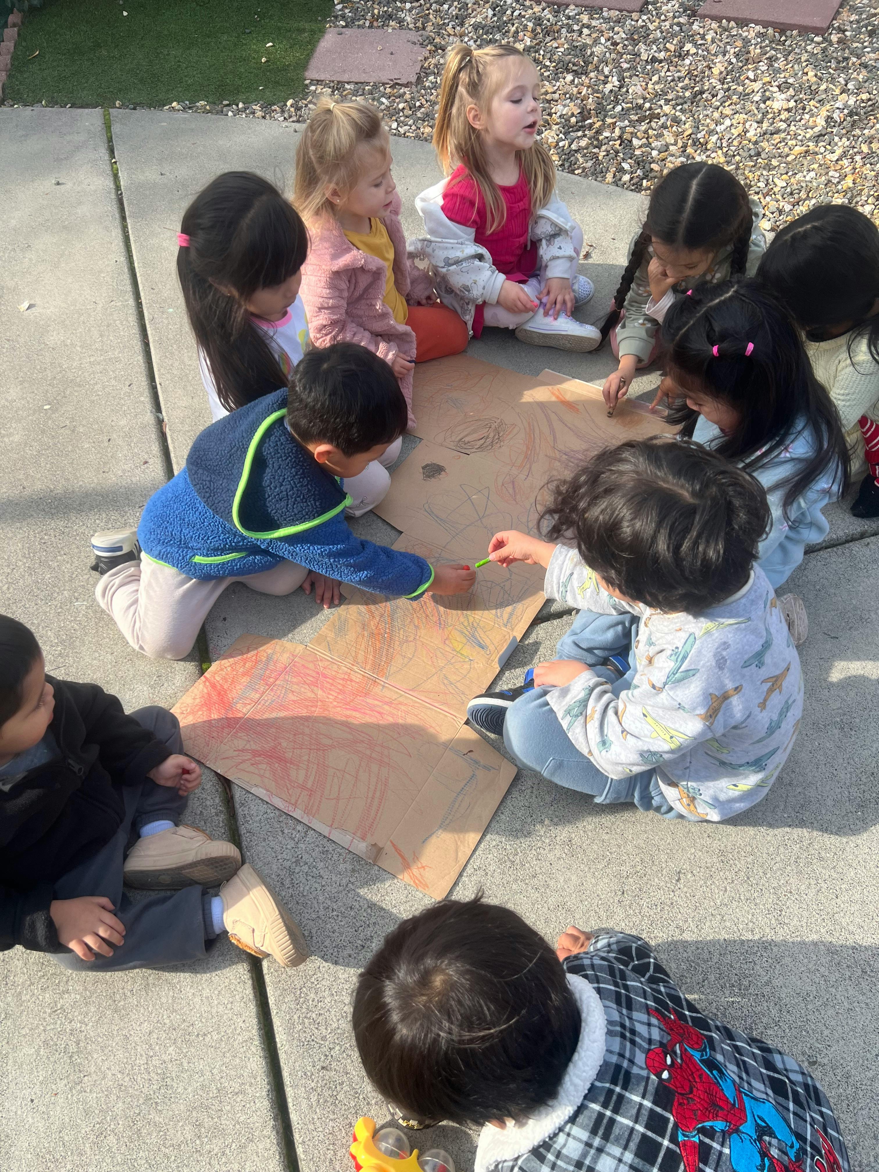 Children sitting on the ground drawing on cardboard