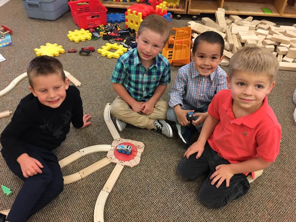 Four children sitting on the floor with a toy train track