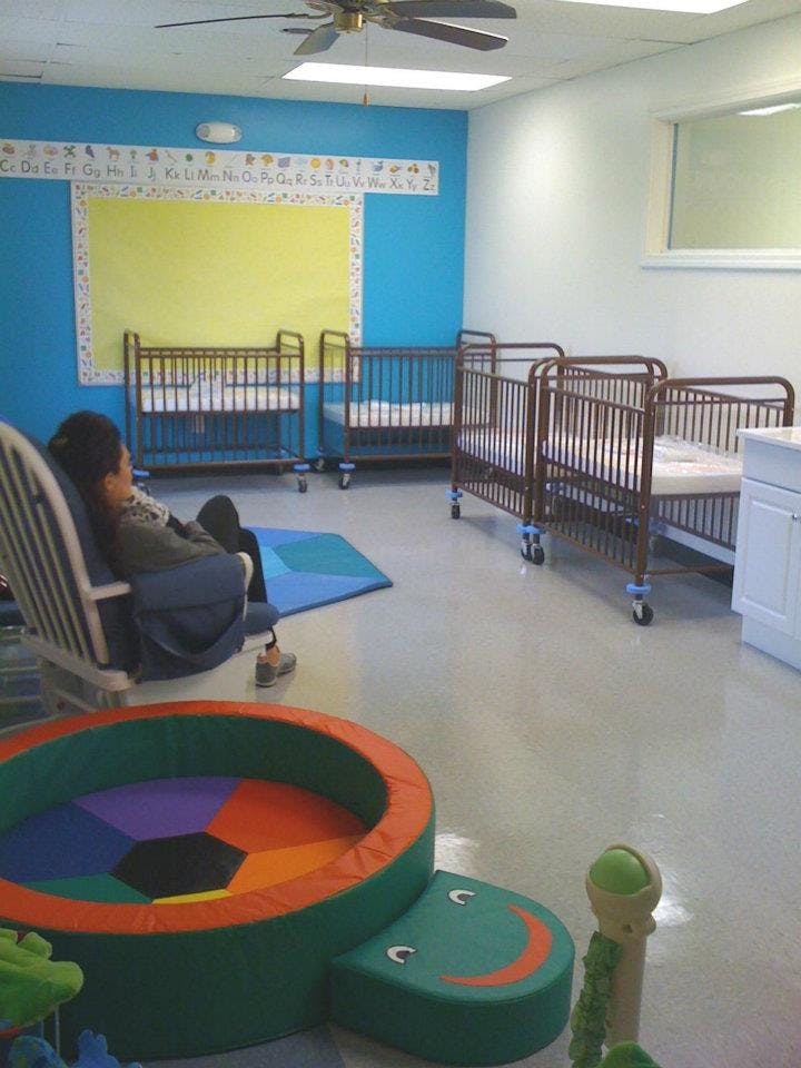 Person sitting in a chair in a room with multiple cribs and play equipment