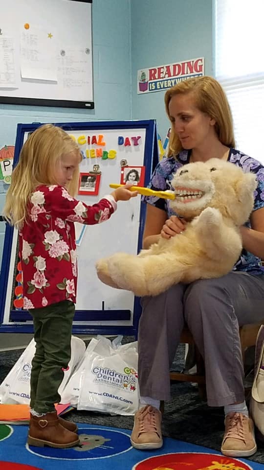Child brushing teeth of a large stuffed animal held by an adult