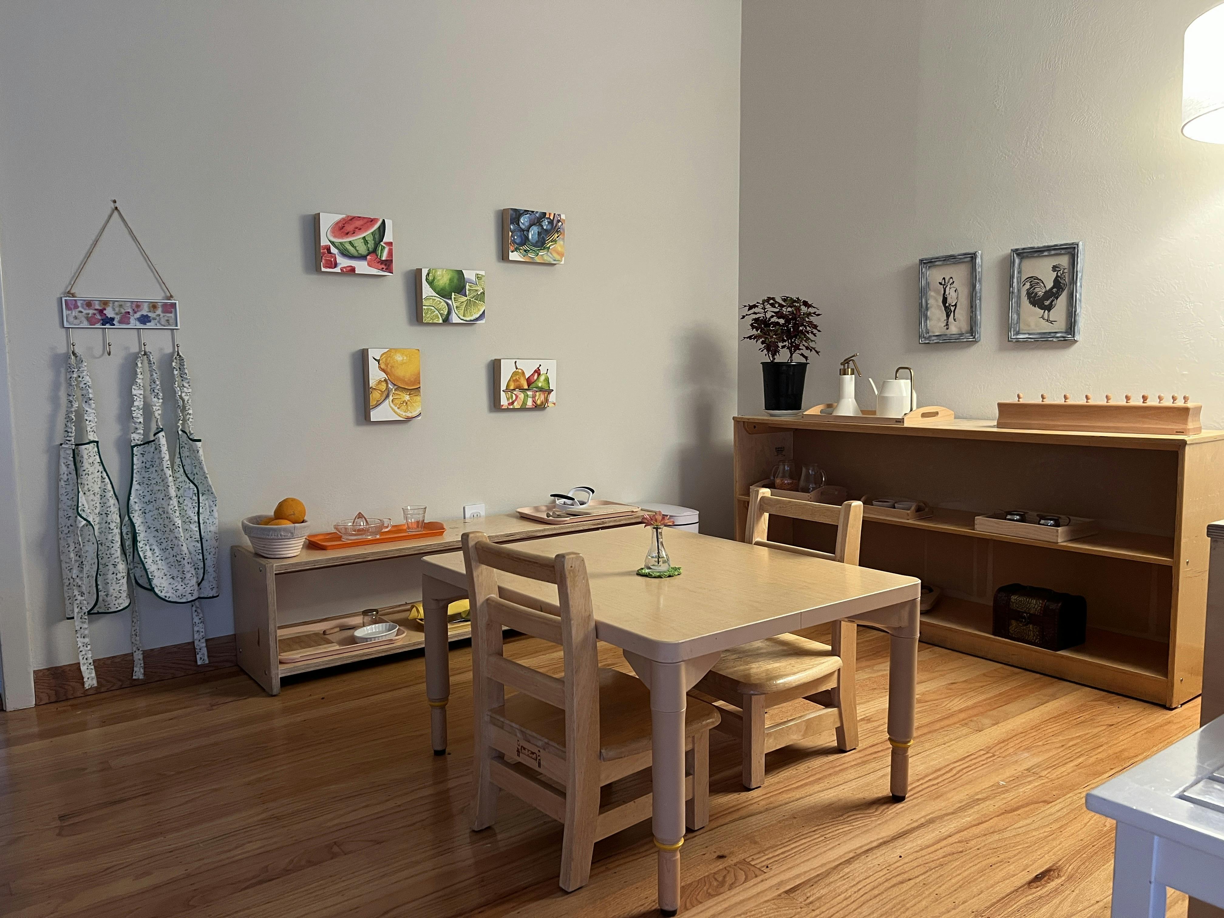 Classroom with small table and chairs, shelves with materials, and fruit art on wall