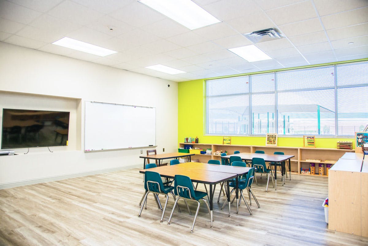 Empty classroom with tables, chairs, whiteboard, and large windows