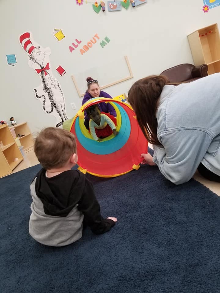 Two adults and two children playing with a colorful tunnel in a classroom