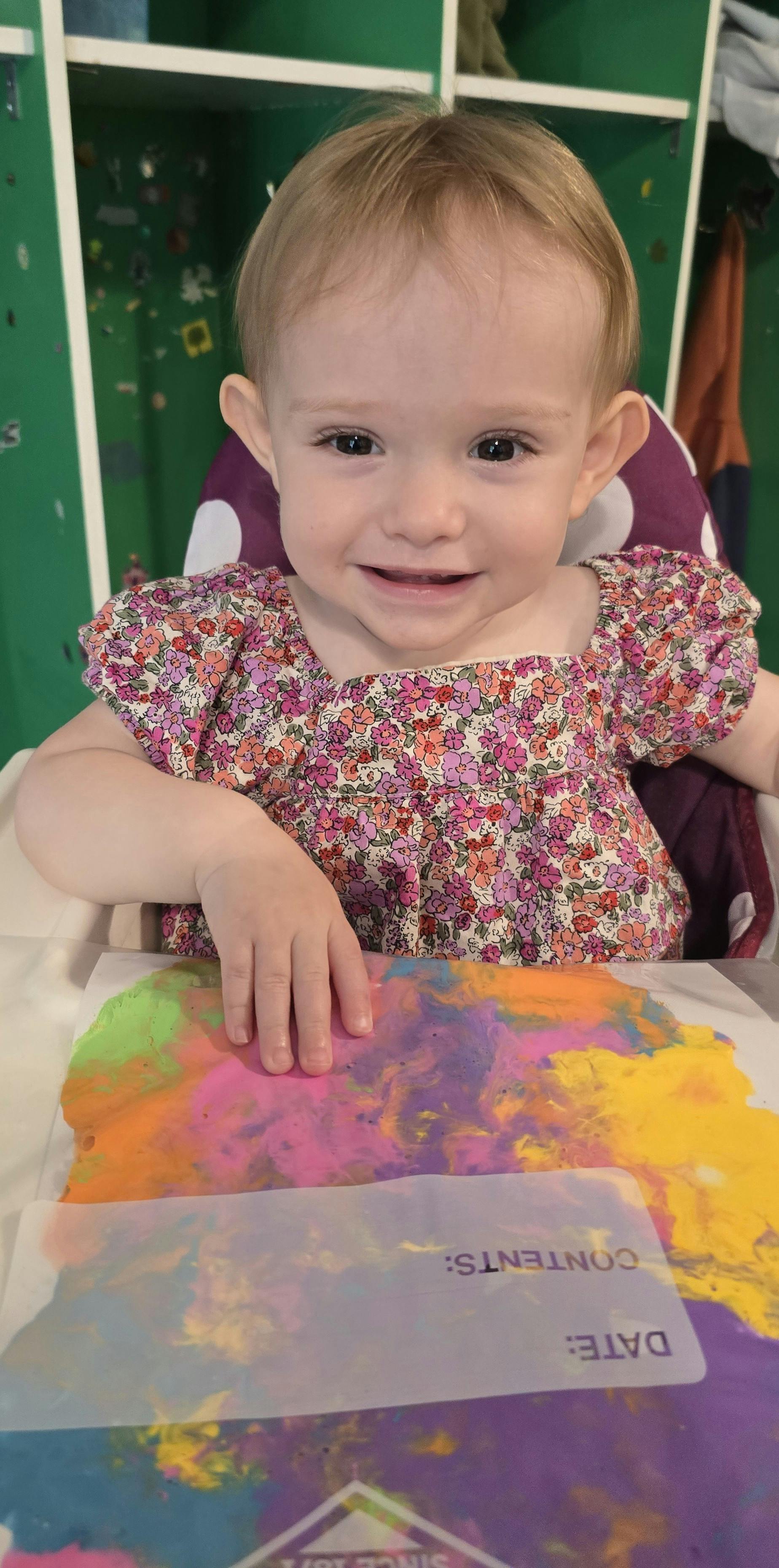 Child in a high chair with hand on colorful art