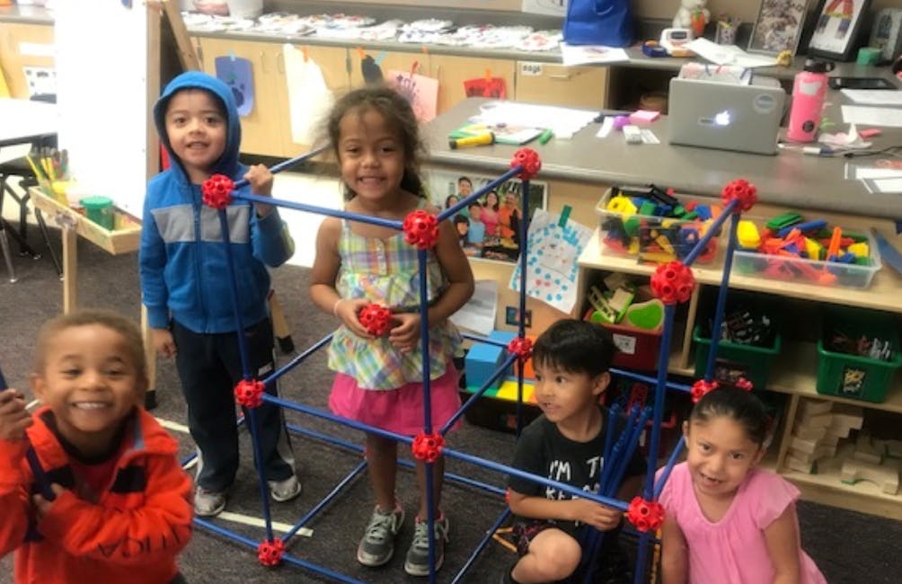 Four children playing with a construction toy in a classroom