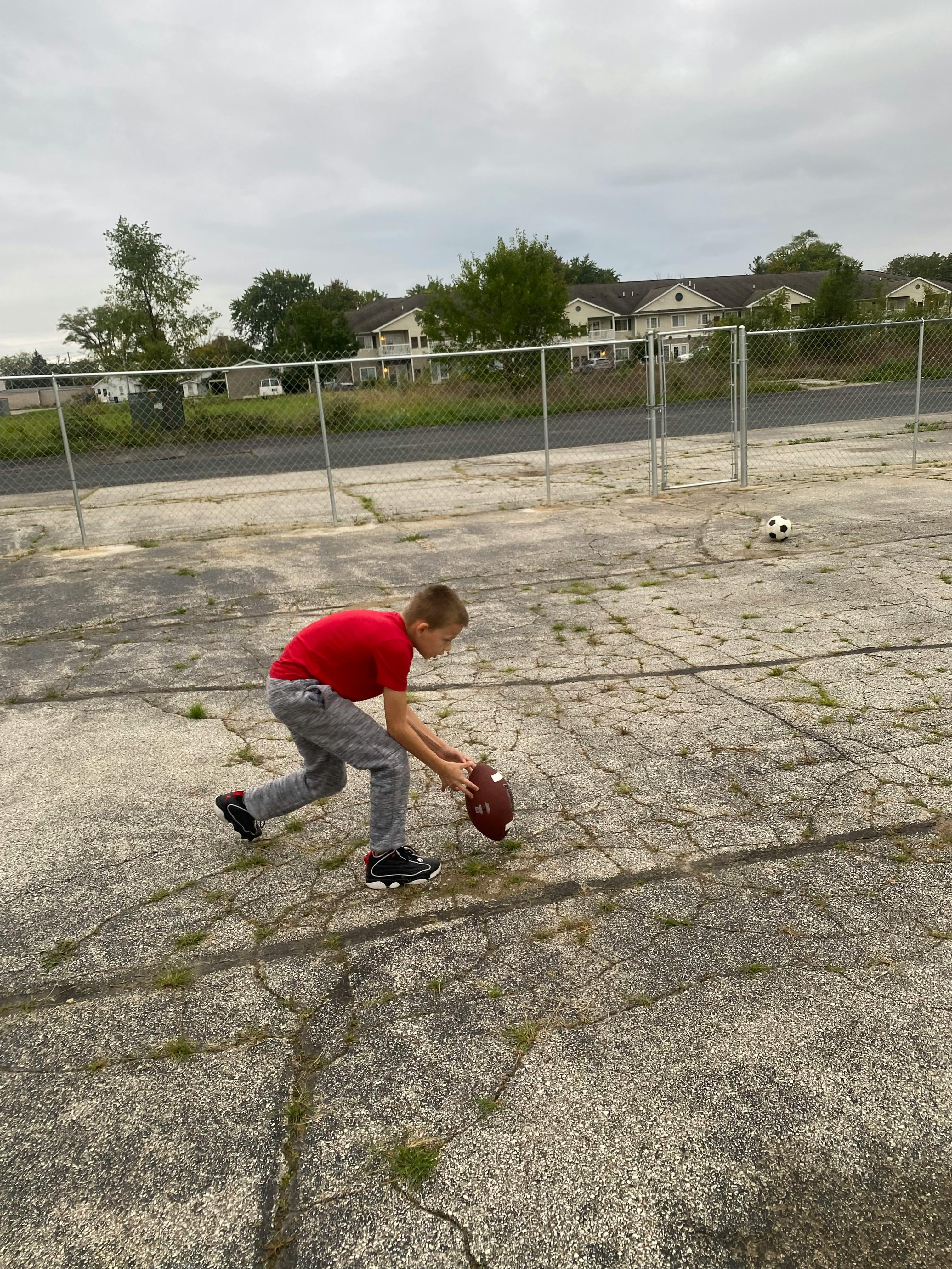 Child in red shirt holding a football on cracked pavement
