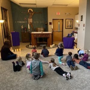 Children and adults sitting on the floor in a room with religious decor