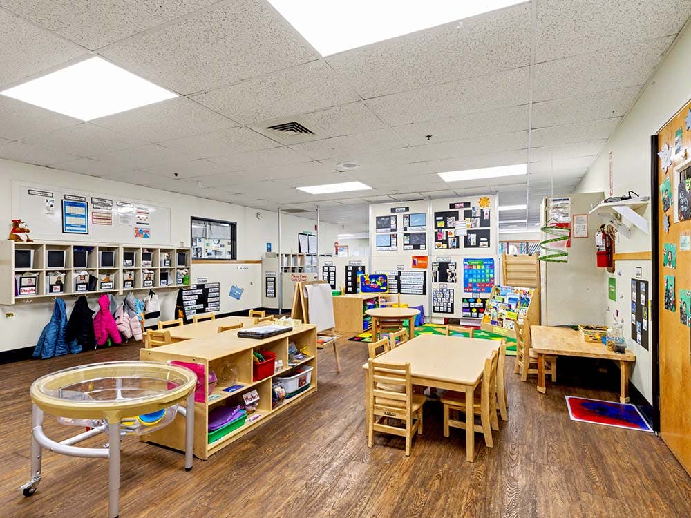 Classroom with small wooden tables and chairs, cubbies, and various learning materials