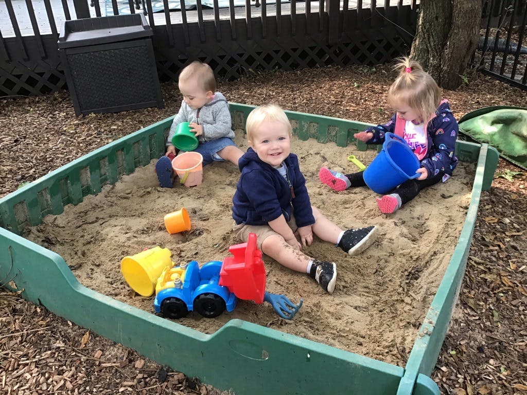Three children playing in a sandbox with toys