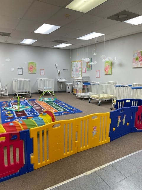 Nursery room with multiple cribs, play mat, and colorful playpen
