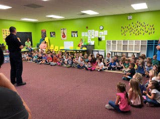 Adult speaking to a group of children sitting on the floor in a classroom