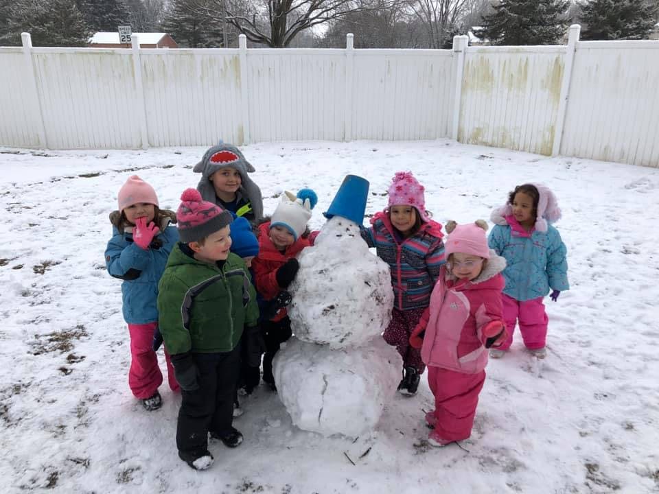 Children standing around a snowman in a snowy yard