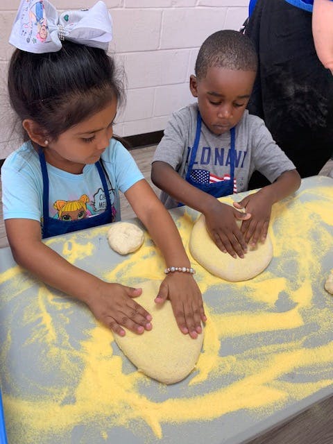 Two children in aprons pressing dough on a floured surface
