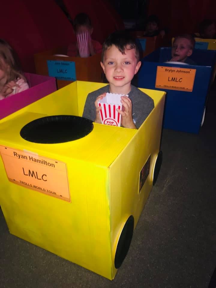 Child in a yellow cardboard car holding a popcorn box