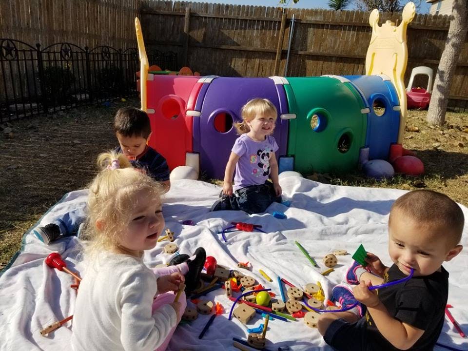 Four children playing with toys on a blanket outdoors