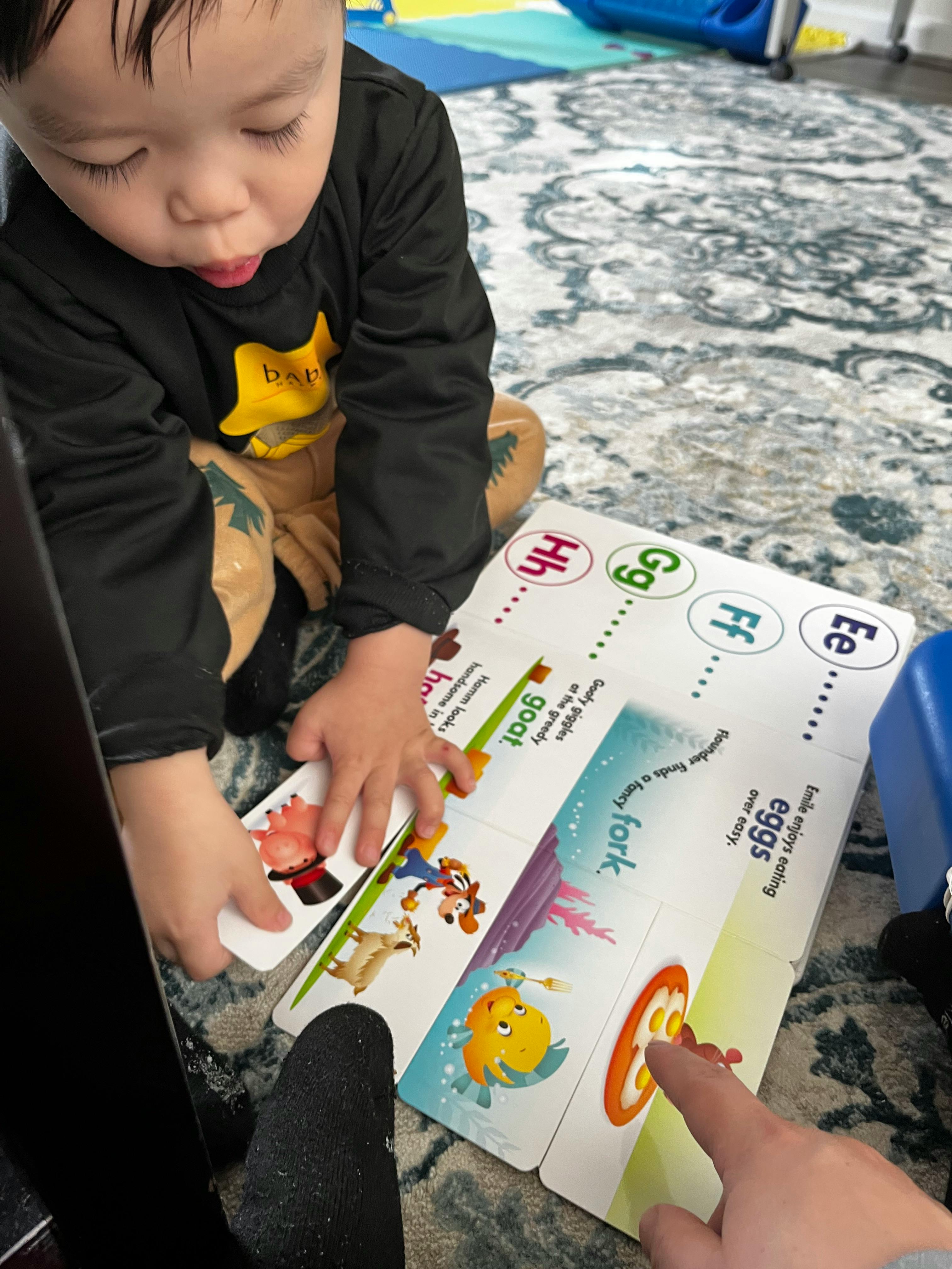 Child looking at a book with a person's finger pointing at it
