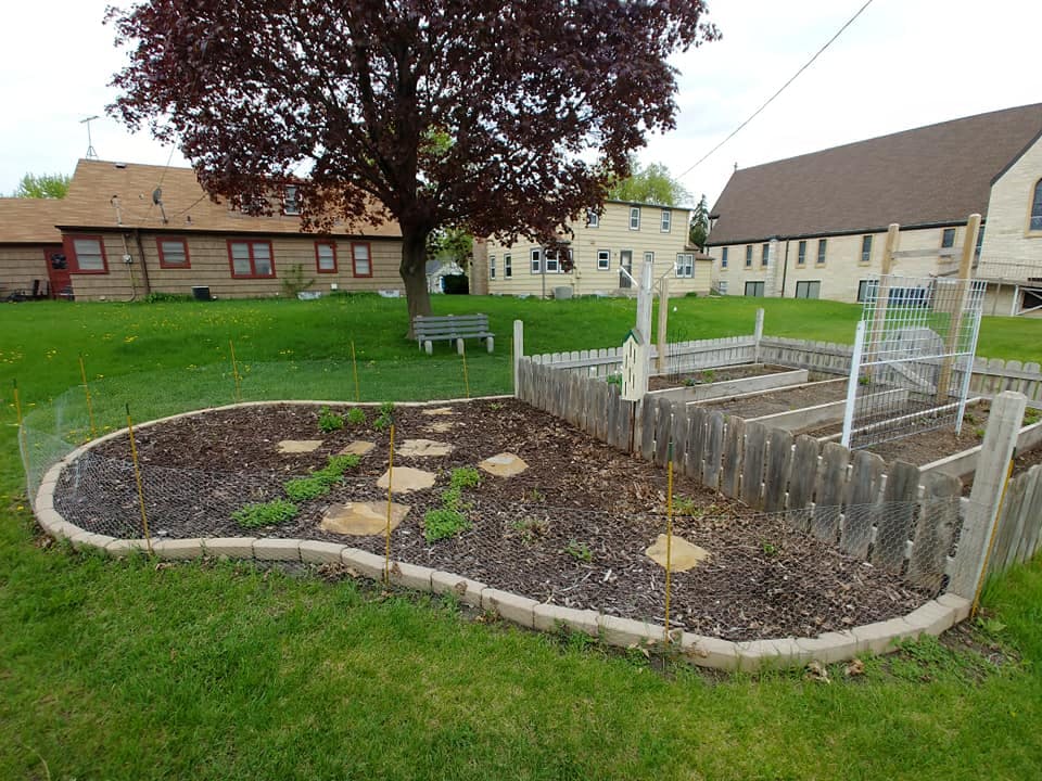 Garden beds with a stone path and a wooden fence