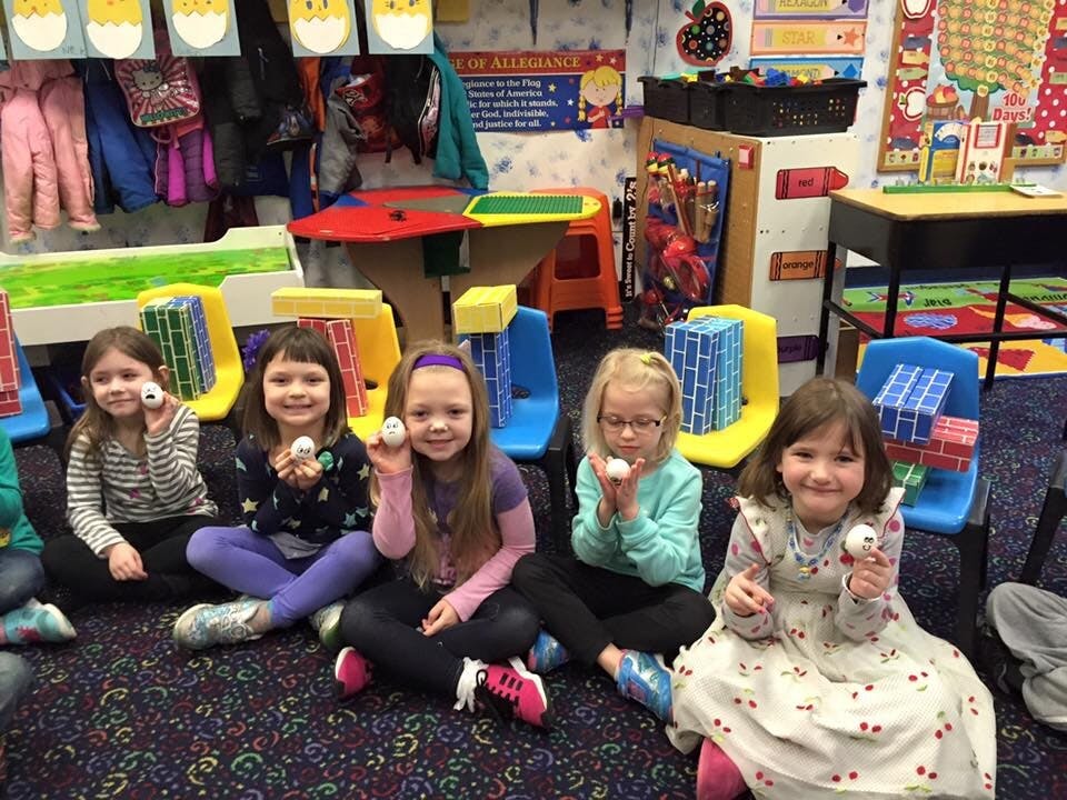 Four children sitting on a floor holding small white objects