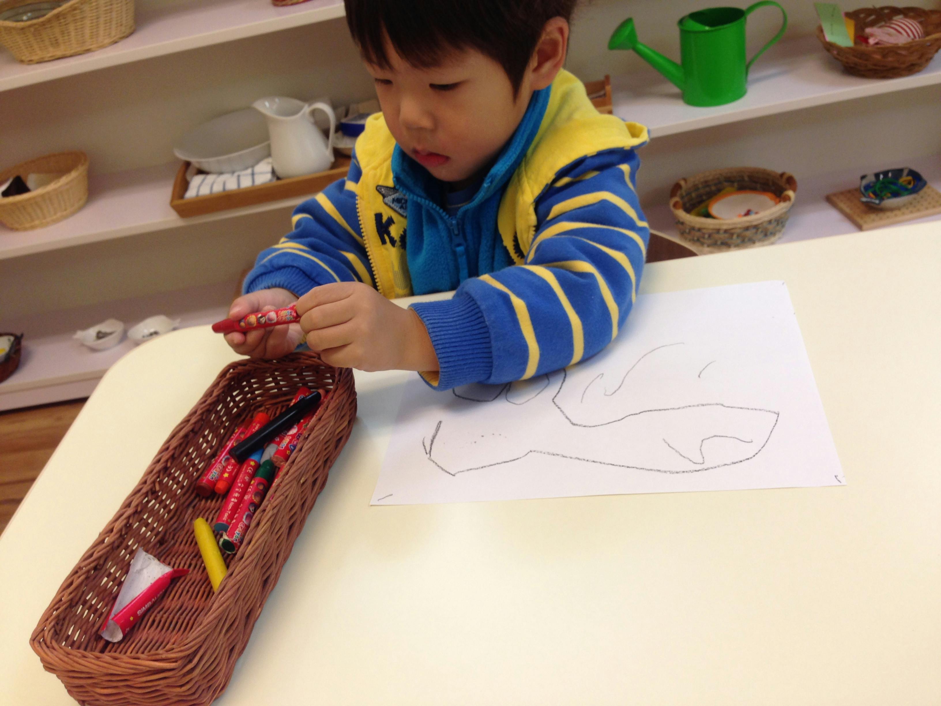 Child drawing on paper with crayons atable and crayons