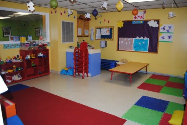 Playroom with colorful mats, small table, and shelves with toys on shelves