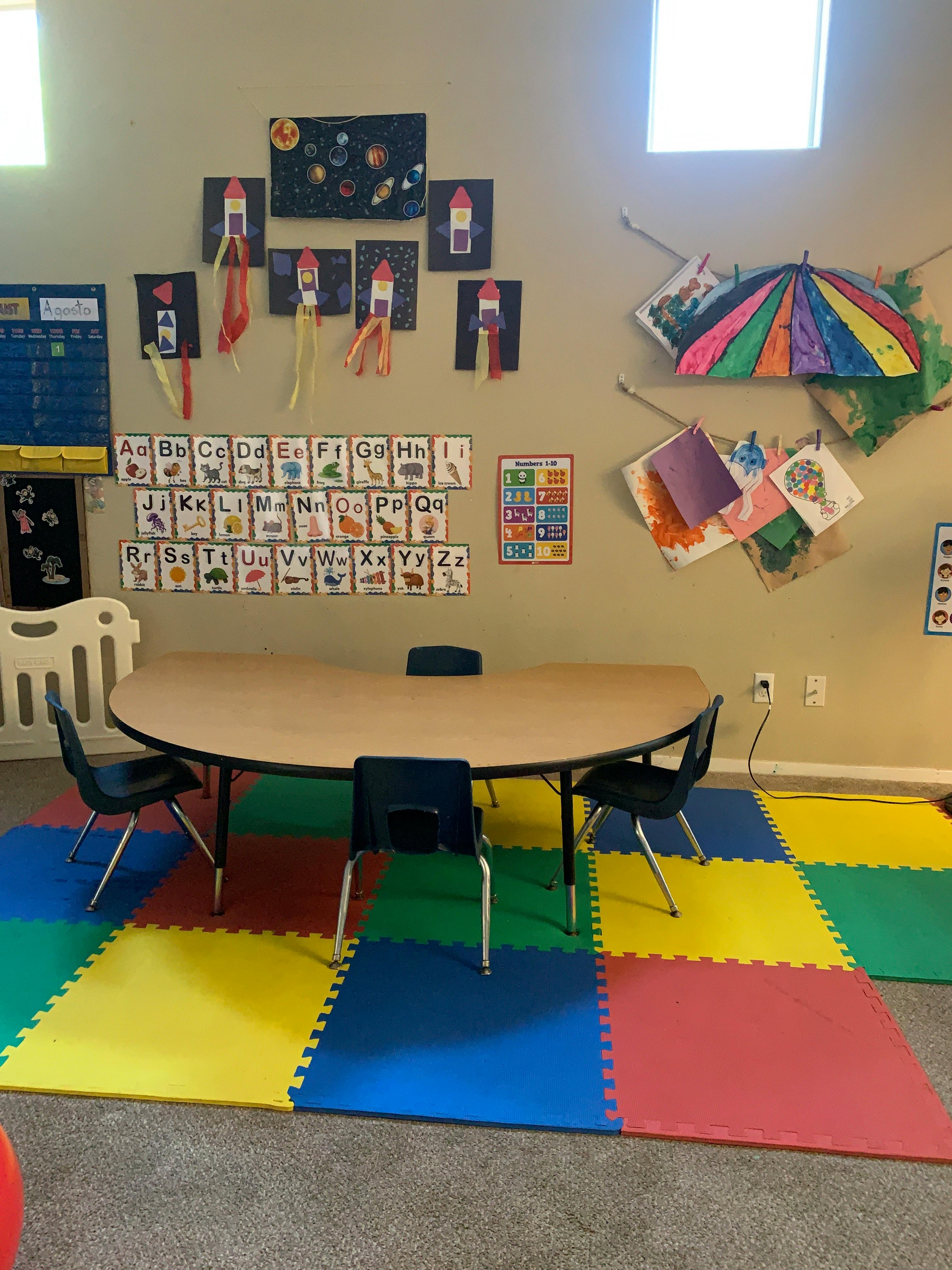 Classroom with a table, chairs, colorful floor mats, and wall decorations