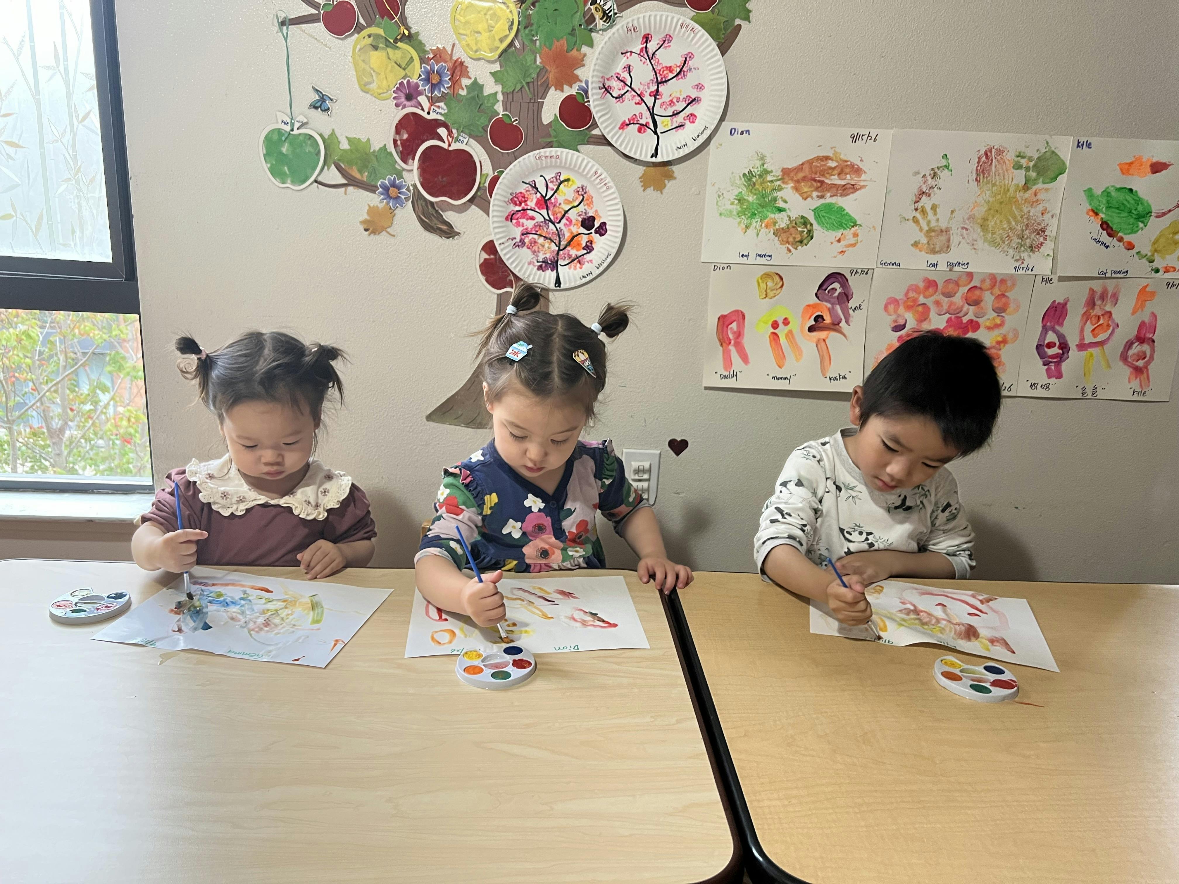 Three children sitting at a table painting with watercolors