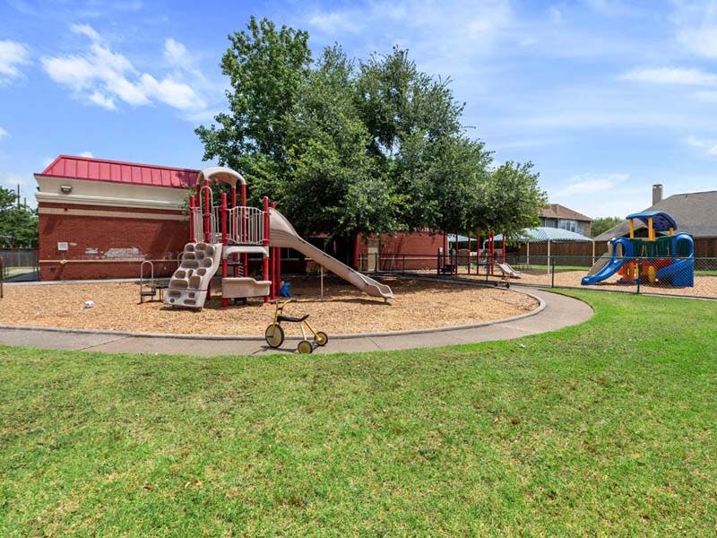 Outdoor playground with slides, climbing structures, and a small tricycle on wood chips