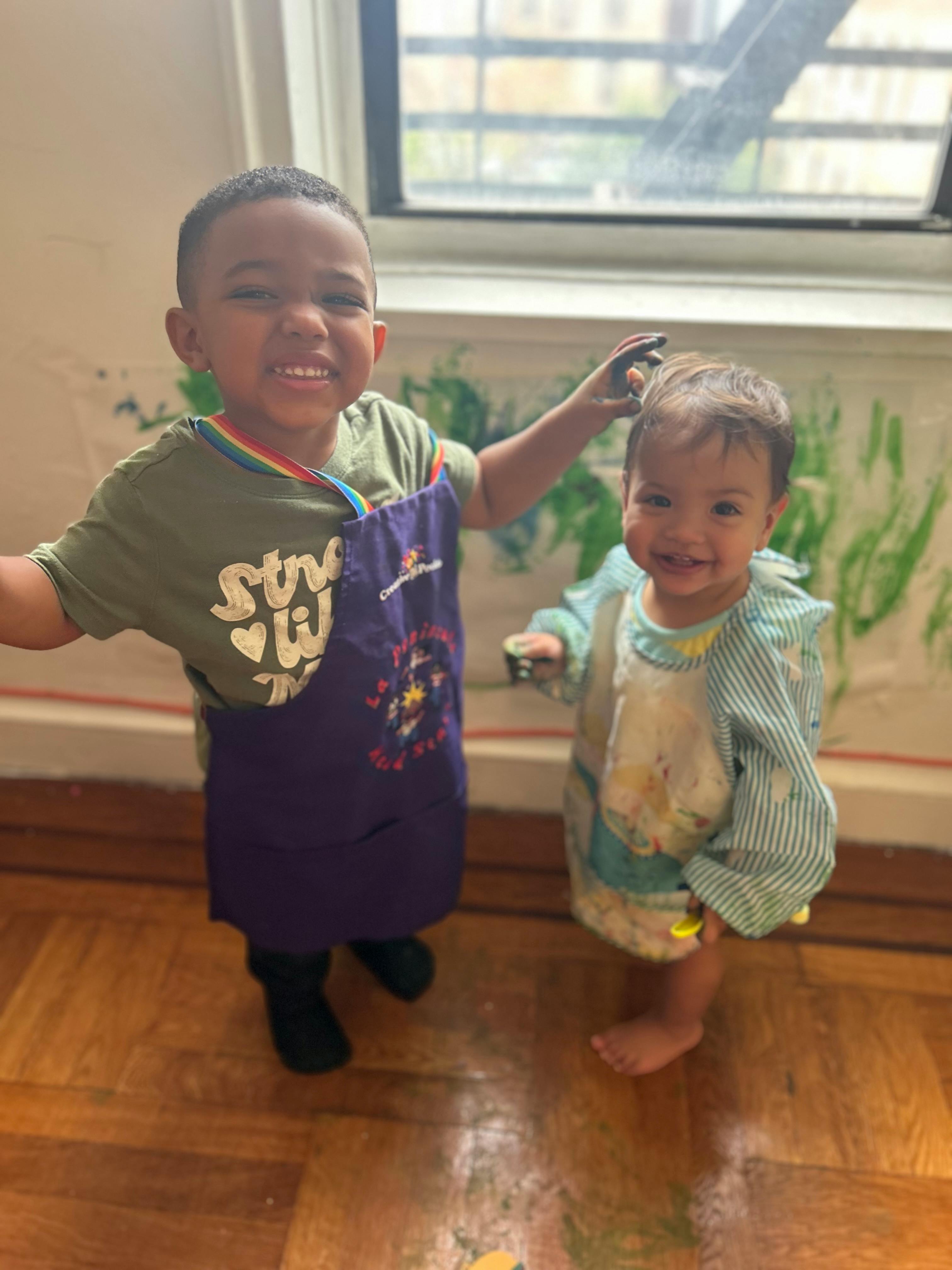 Two children in aprons, one with paint on their head