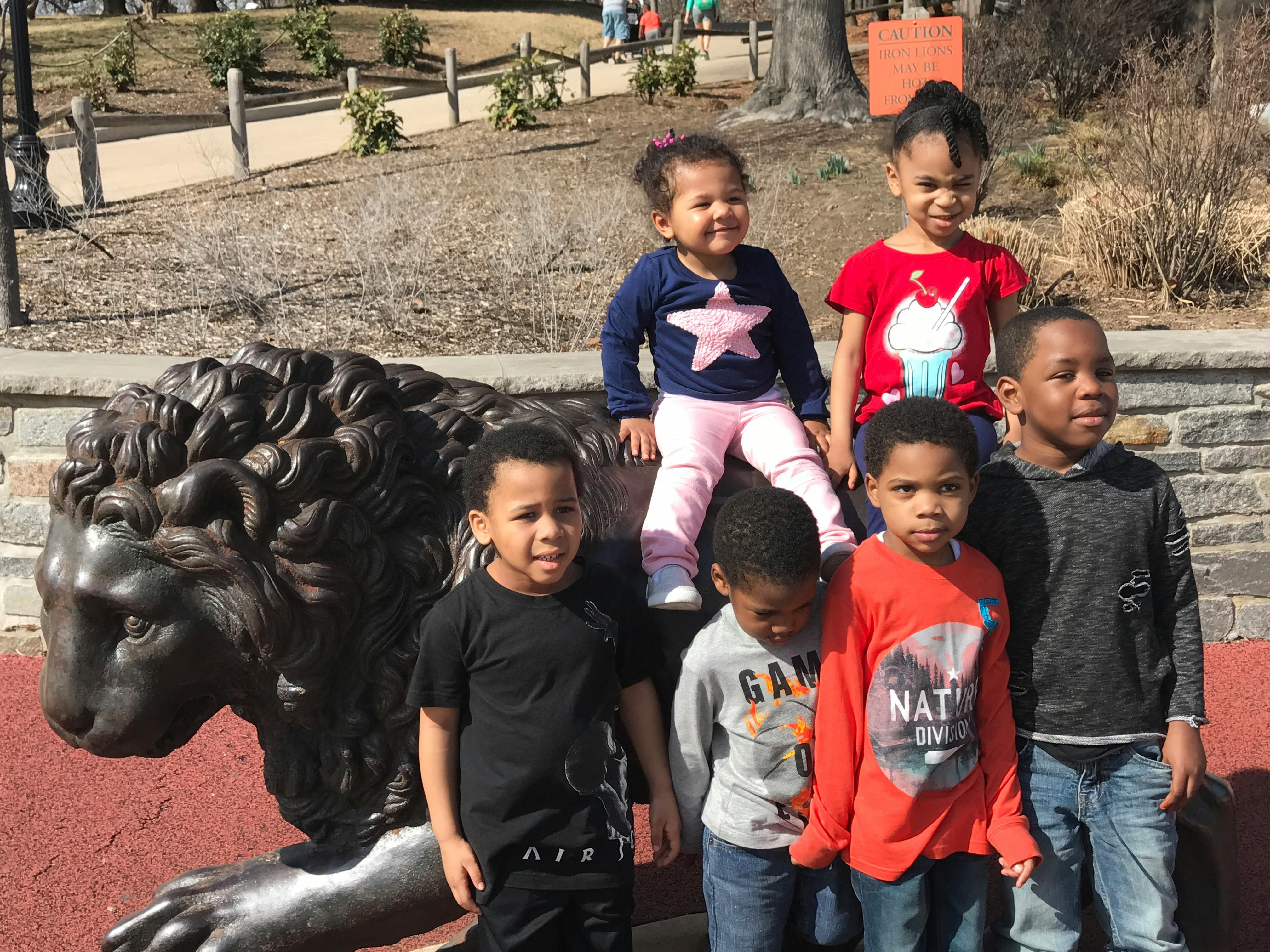 Group of children posing near a large metal lion statue