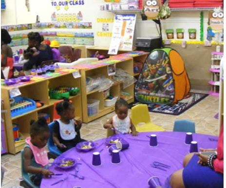 Children sitting at a table with purple tablecloth and cups in a classroom