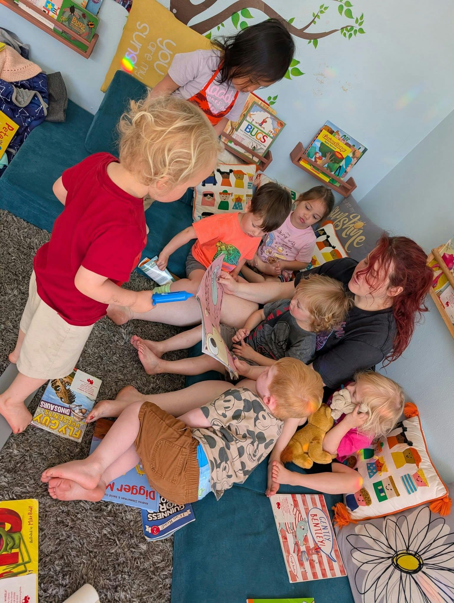 Adult and multiple children reading books on the floor